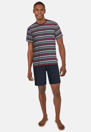 Kurzarm gestreiftes Hemd in Grau, Navy und Bordeaux; kombiniert mit einfarbigen Navy-Shorts. Weicher Stoff, lockere Passform, barfuß getragen.