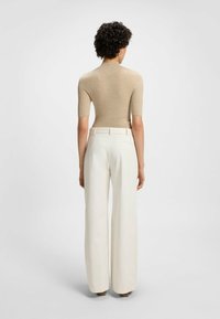 Beige geripptes Kurzarmoberteil, kombiniert mit hoch taillierten, weit geschnittenen weißen Hosen. Glatte Textur und neutrales Farbschema.