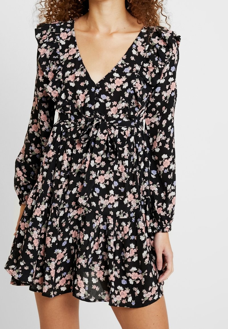 Černé květinové šaty s dlouhými rukávy, volány na ramenou, výstřihem do V, nařaseným pasem a vícevrstvou sukní s drobnými růžovými a modrými květy.