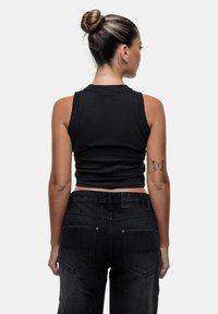Top corto nero con design aderente, abbinato a jeans neri a vita alta. Presenta dettagli di cucitura sul retro e tasche posteriori.