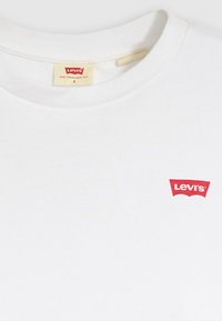 Baltas medvilninis marškinėlis su raudonu Levi's logotipu ant krūtinės, klasikinio apvalios apykaklės ir trumpomis rankovėmis. Lygus audinys.