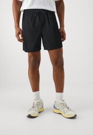 Zwarte zwemboxers met elastische tailleband en trekkoord. Gecombineerd met witte sportsokken en multifunctionele sneakers. Glad textuur van de stof.