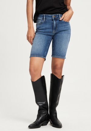 Dżinsowe szorty w średnim niebieskim kolorze, o dopasowanym kroju, wykończone podwiniętym dołem. Zestawione z czarnymi skórzanymi butami za kolano.