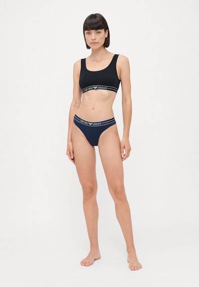 Zwarte sport-bh en bijpassende string met contrasterende witte "Emporio Armani" logo banden. Glad materiaal met een aansluitend ontwerp.