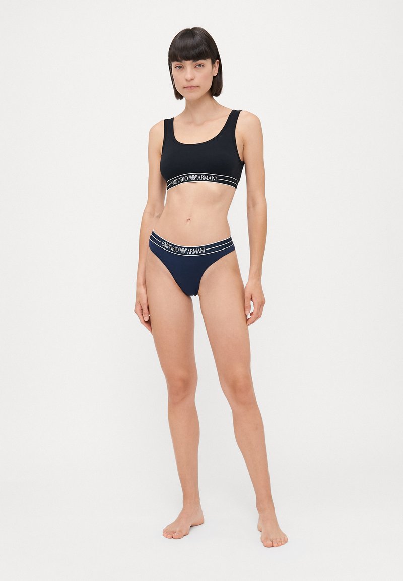 Zwarte sport-bh en bijpassende string met contrasterende witte "Emporio Armani" logo banden. Glad materiaal met een aansluitend ontwerp.