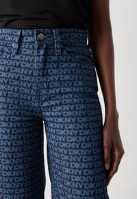 Jeans aus Denim in einem dunklen Blau mit einem wiederholten hellblauen "DKNY"-Logo-Muster, mittlerer Bundhöhe und figurbetonter Silhouette.
