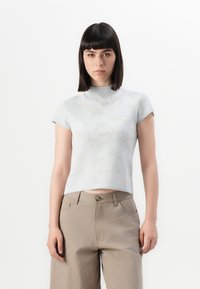 Lyseblå strikket topp med korterm, høyt krage, med et subtilt blomsterdesign, kombinert med beige høy-midje bukser.