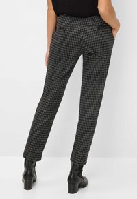 Geprinte broeken in een zwart-grijs houndstooth ontwerp, met een getailleerde pasvorm, zijzakken en een soepele textuur. In combinatie met hoge laarzen.