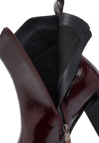 Stivale alla caviglia bordeaux lucido con interno in pelle nera e chiusura con cerniera. Presenta una superficie texturizzata e un design senza cuciture.