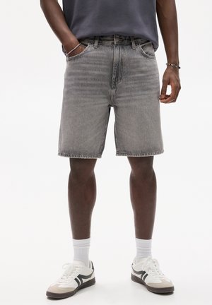 Personne portant un short en jean gris délavé mi-long, un t-shirt gris foncé, des chaussettes blanches et des baskets blanches avec des accents noirs.