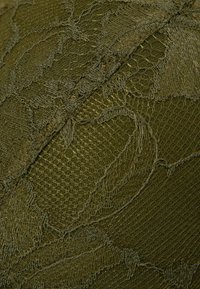 Gestructureerde olijfgroene stof met ingewikkelde kantpatronen en gaas, die verschillende oppervlakdetails en een zachte afwerking benadrukt.
