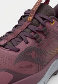 Maroon athletic shoe with textured fabric upper, reinforced toe, and intricate side patterns. Features flat laces and contrast accents.