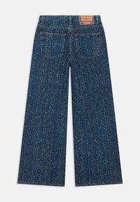 Jeans en denim à jambes larges de couleur bleu foncé avec une surface texturée, présentant des poches arrière et une étiquette de marque contrastante sur la ceinture.