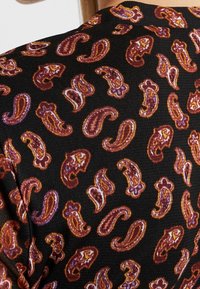 Svart tyg med ett paisleymönster i nyanser av bordeaux, orange och lila. Struktur med en slät yta.