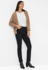 Cardigan a maglia marrone chiaro con bottoni, t-shirt bianca, jeans scuri e stivaletti neri con tacco. Texture liscia con polsini arrotolati.