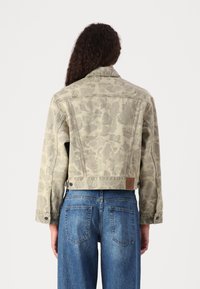 Afskåret denimjakke i lys grøn med et subtilt blomstermønster. Har krave, lange ærmer og et mærket lædermærke på bagsiden.