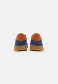 Blaue Wildledersneaker mit orangefarbenen Fersenakzenten, runder Spitze, strukturiertem sandfarbenem Außensohle und Markenzeichen-Detail an der Ferse. Lässiger Stil, Rückansicht.