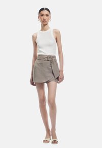 Top sin mangas blanco acanalado combinado con una falda envolvente beige con un nudo decorativo y cinturón, complementado con zapatos de tacón abierto.