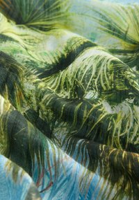 Tkanina s detaljnim uzorcima zelenih i plavih tropskih listova, prikazujući nabore i teksturu u mekanom, laganom materijalu.