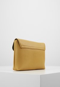 Żółta skórzana kopertówka o fakturowanej powierzchni, prostokątnym kształcie i klapce jako zapięciu. Minimalistyczny design bez dodatkowych zdobień.