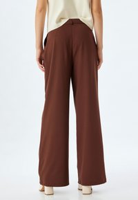 Wide-leg brown trousers made of lightweight fabric, featuring a smooth texture, high waistband, and side pockets. Subtle drape enhances fit.