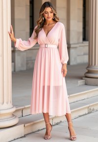 Jasnoróżowa maxi sukienka z przezroczystego materiału, z dekoltem w serek, długimi rękawami, paskiem w talii z kwadratową klamrą i zwiewnym dołem.