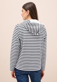 Sudadera a rayas con líneas horizontales en blanco y negro, tela suave, capucha adjunta y mangas largas, combinada con vaqueros azules.