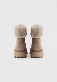 Bottes en suédine beige avec un revers en fausse fourrure fluffy, marron clair et des semelles épaisses et texturées, mettant en avant un design robuste et une palette de couleurs neutres.