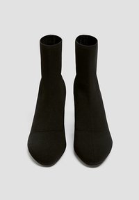 Bottines noires en tissu extensible avec une texture lisse. Bout pointu et un design épuré et sans couture, adaptées à diverses occasions.