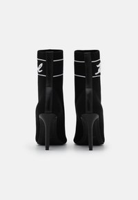 Botines de punto negros hasta el tobillo con un diseño tipo calcetín, tacones altos de aguja y detalle del logo en blanco en el cuello. Acabados de cuero suave en la parte trasera.