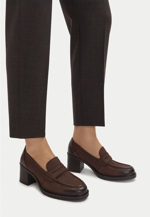 Mocasines de cuero marrón con tacón bloque y punta redondeada, con un panel frontal cosido y diseño minimalista. Textura suave, estilo clásico.