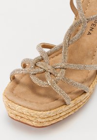 Beige kilehæle sandal med en tekstureret espadrille-platform, der har funklende sammenflettede stropper og en blød ruskinds sål.
