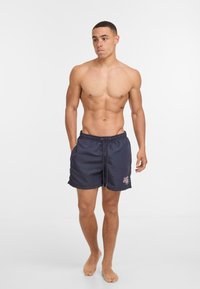 Jūras zila peldbikses izgatavotas no gludas auduma ar elastīgu jostu, ar kontrastējošu rozā logotipu priekšā un brīvu piegriezumu.