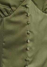 Olivno zelena satenska obleka z usklajenim korzetom, ki ima vrsto šestih gumbov oblečenih v tkanino in nabran občutek na eni strani.