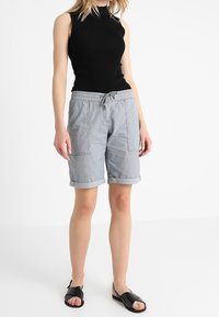 Szare spodenki w paski z podwiniętymi nogawkami i przednimi kieszeniami, połączone z czarną bezrękawniką i czarnymi sandałami. Lekki materiał, casualowy fason.