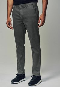 Grå bomuldsblandingsbukser med slim fit, flad front og sidelommer, kombineret med sorte atletiske sko. Subtile stikdetaljer.