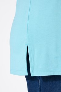 Hellblauer Stoff mit seitlichem Schlitz-Detail, getragen über dunkelblauen Jeans.