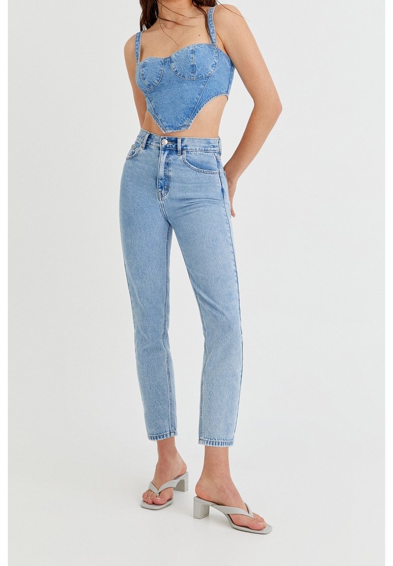 Top corto de mezclilla azul con escote corazón, jeans de tiro alto de color azul claro y sandalias de tacón bloque gris. Ajuste casual, acentos mínimos.