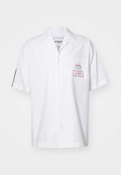 Short-sleeve white shirt made of cotton with a button closure. Features a chest pocket with a red label, and a classic collar design.