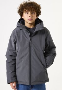 Chaqueta impermeable gris con cremallera frontal, capucha ajustable y bolsillos laterales. Presenta una tela texturizada y un diseño de corte relajado.