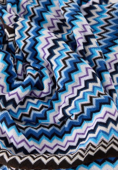 Tissu tricoté doux avec un motif en zigzag dans des tons de bleu, violet, noir et blanc, présenté en plis et en gros plan sur la texture.