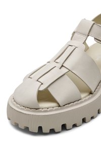 Sandale en cuir beige avec semelle épaisse rainurée, bout ouvert et larges brides sur le pied et la cheville avec détails cousus.