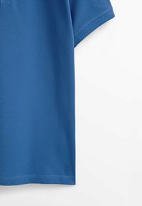 T-shirt en coton bleu à manches courtes avec un petit logo brodé près de l’ourlet inférieur sur fond blanc.