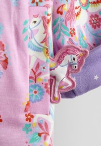 Audums ar daudzkrāsainiem ziedu un vienradža rakstiem rozā un violetās toņos, ar uzšūtu vienradža uzlīmi uz kabatas malas.