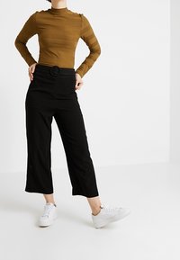 Brun ribbad långärmad topp i kombination med höga svarta cropped byxor med ett runt bälte. Bärs med vita sneakers.