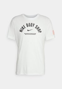 Biała koszulka z bawełny z napisem "NIKE BODY SHOP" w czarnym kolorze, małym logo Nike oraz wzorem w szachownicę poniżej napisu.