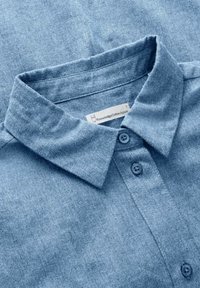 Light blue denim shirt with a classic collar, two buttons, and a textured fabric. Label reads "Knowledge Cotton Apparel."