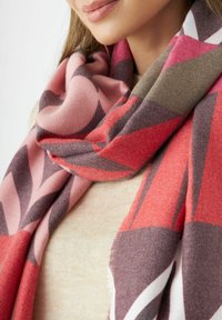 Textured sjaal in tinten van roze, rood en grijs, met hoekige geometrische patronen. Zacht materiaal met franjes voor een extra detail.