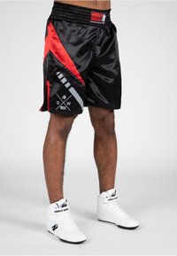 Zwarte satijnen sportshorts met rode accenten, voorzien van geometrische patronen en een logo op de zijkant, een elastische tailleband en een gladde afwerking.
