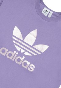 Felpa viola realizzata in tessuto morbido, caratterizzata da un grande logo Adidas bianco e un design con tre strisce. Stile classico con collo rotondo.